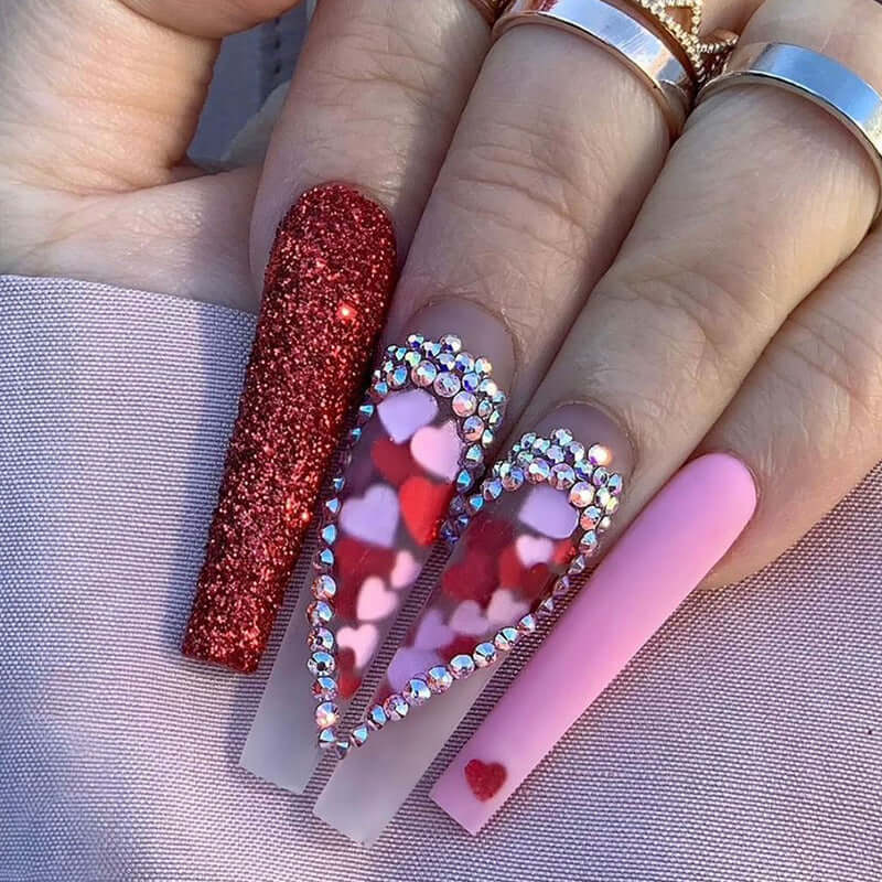 Intricate red and pink nail designs with glitter, hearts, and rhinestones showcasing creative nail art.