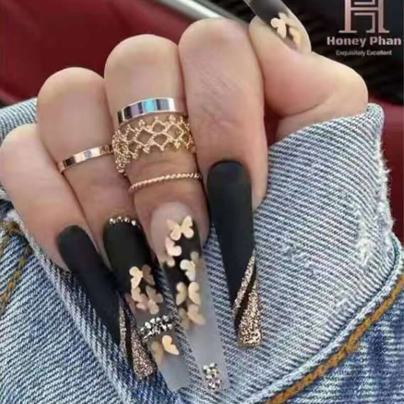 Stylish long nails with golden butterfly designs and rings against a denim background.