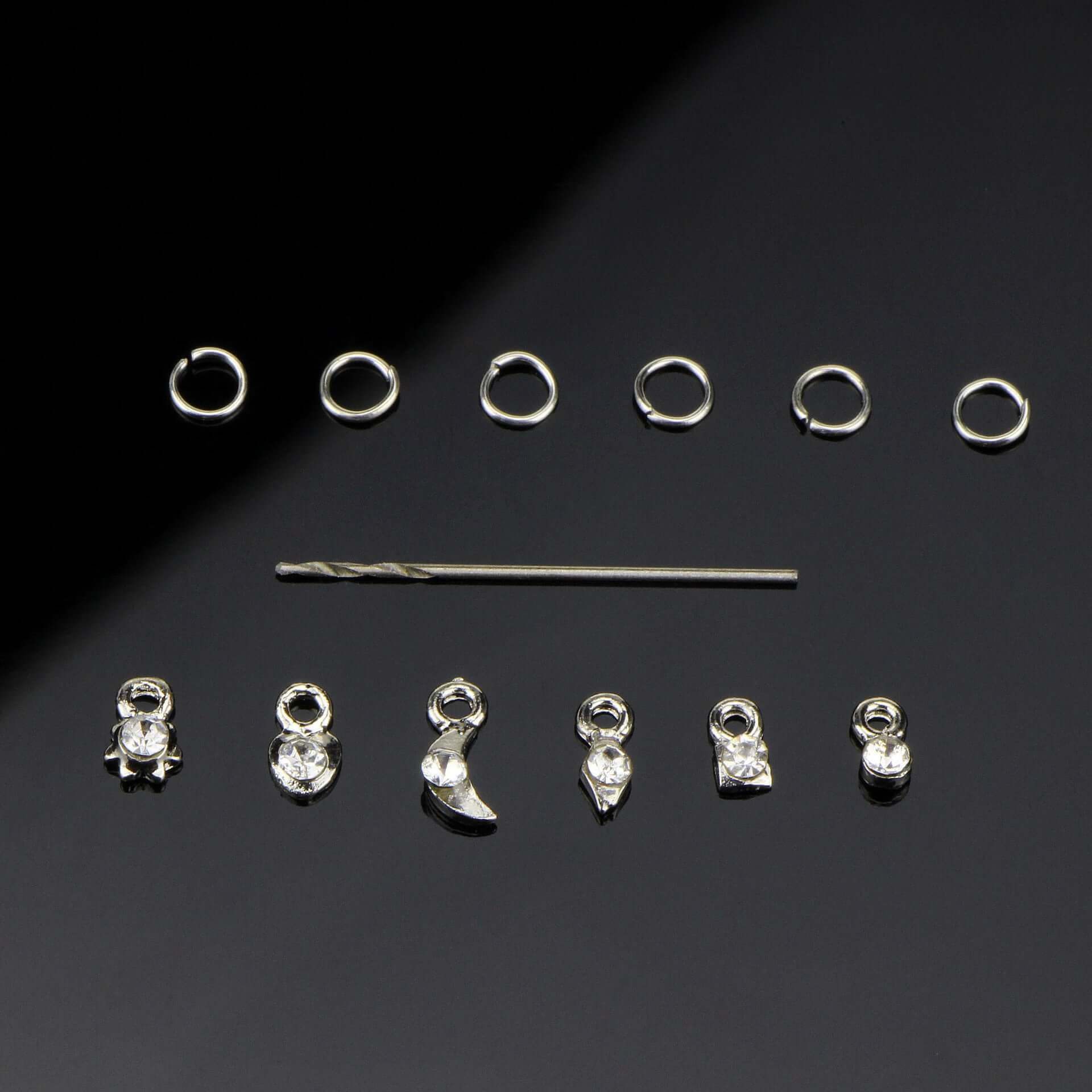 Silver and gold nail art accessories featuring charms, beads, and a toothpick for DIY nail designs.