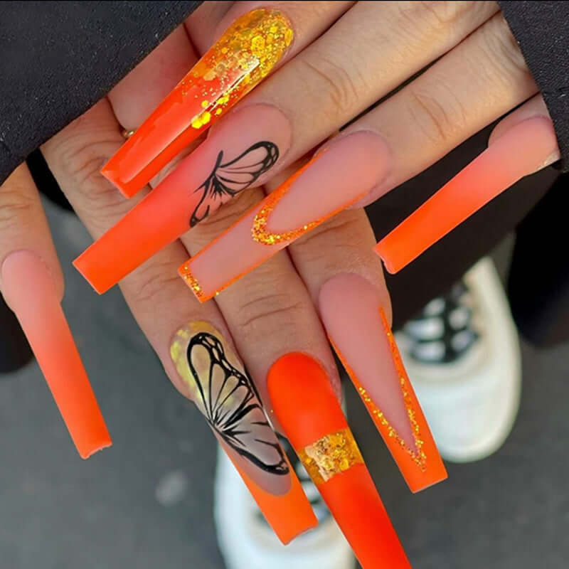 Vibrant orange long acrylic nails featuring butterfly design and glitter, showcasing stylish nail art for creative looks.