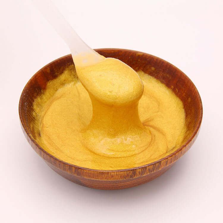 Golden hydrogel jelly mask powder in a wooden bowl with a spatula for skincare treatments.