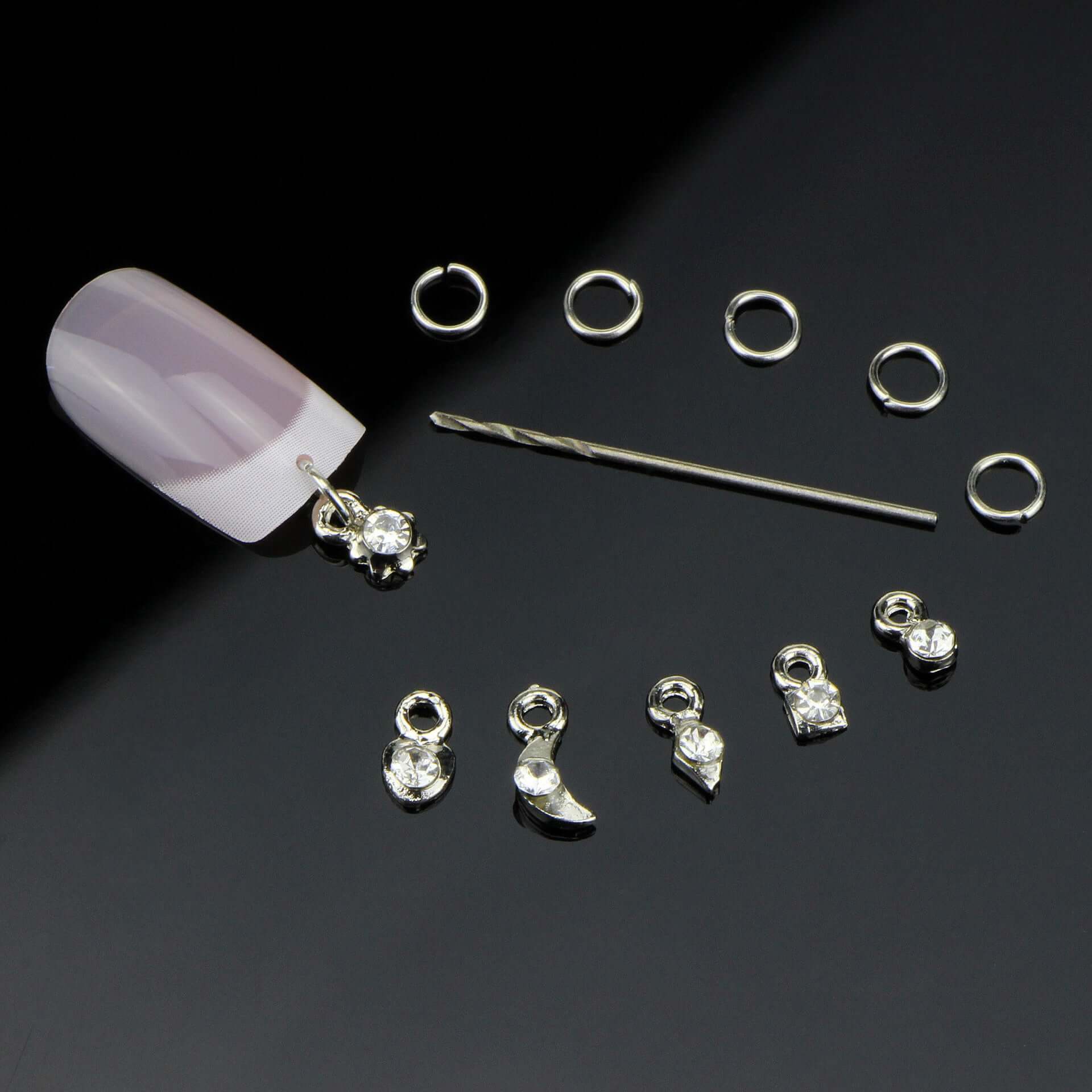 Nail accessories including silver charm straps, rhinestones, and tools for DIY nail art on a black background.