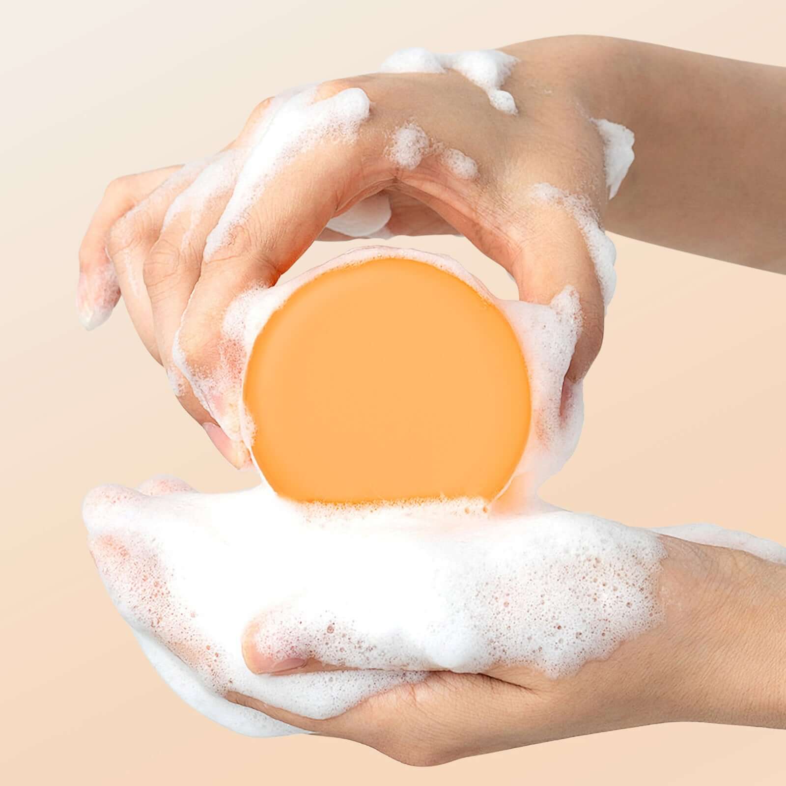 Hands holding a round orange turmeric soap bar lathering with bubbles for moisturizing face wash.